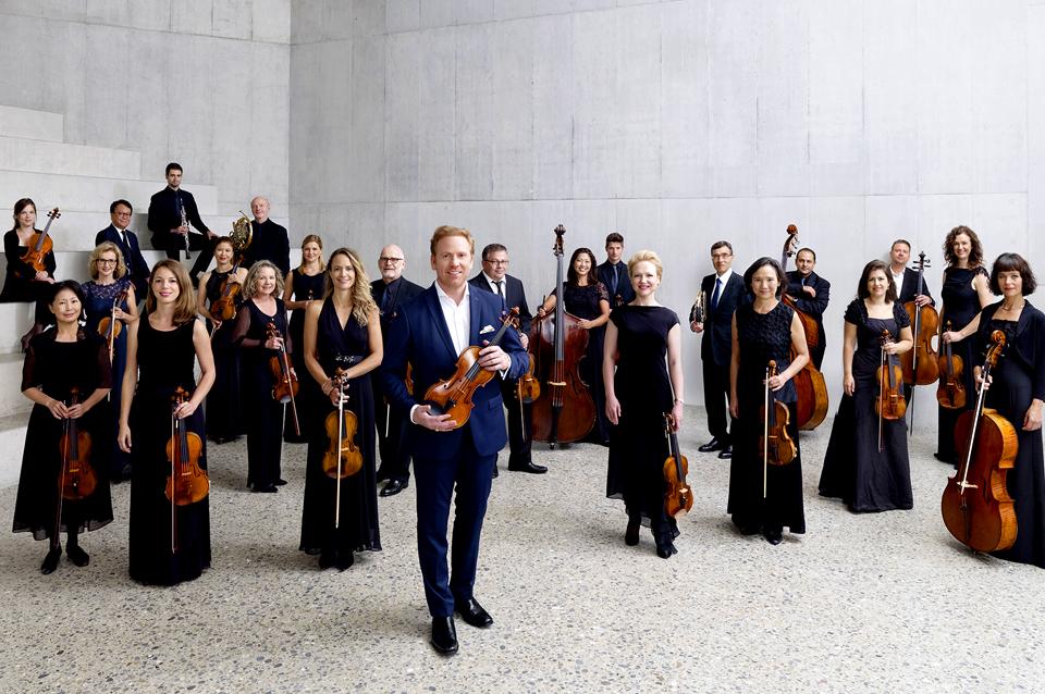 The orchestra members standing in a marble-clad room holding thier instruments.