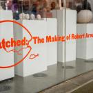 Red letters on a window display announce "Hatched" an art installation inside the lobby of the Manetti Shrem Museum. The photo showcases the exterior window and the small maquette sculptures that modeled Robert Arneson's Egghead sculptures.